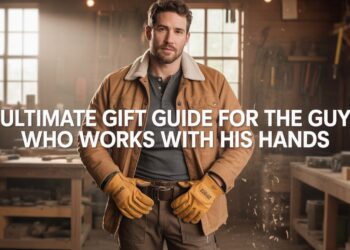 Man in waxed-canvas jacket and leather gloves standing in a workshop, surrounded by tools and wood shavings—visual for ‘Gift Guide for the Hands-On Guy.’