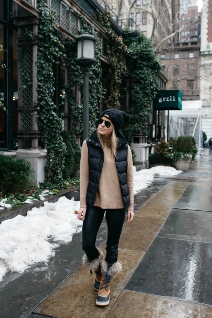 Woman wearing Sorel Joan of Arctic winter boots with faux fur trim, styled with jeans and a winter coat in snowy weather.